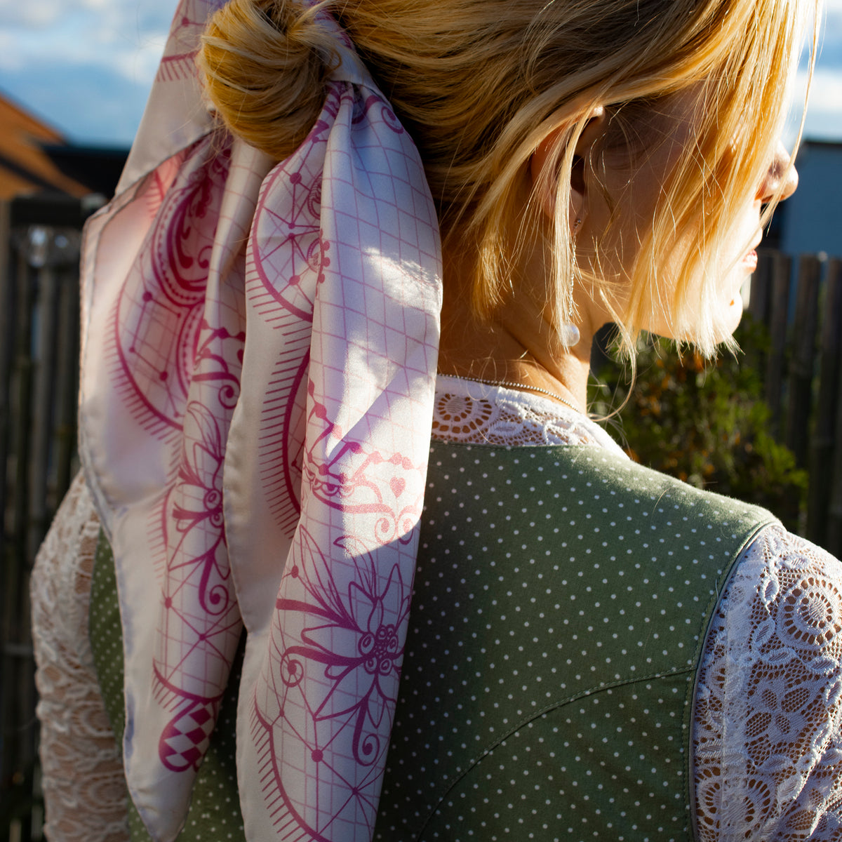 Frau im grünen Dirndl mit Spitzenbluse trägt das Horse Festivity Seidentuch in Blush um den Haarknoten gebunden